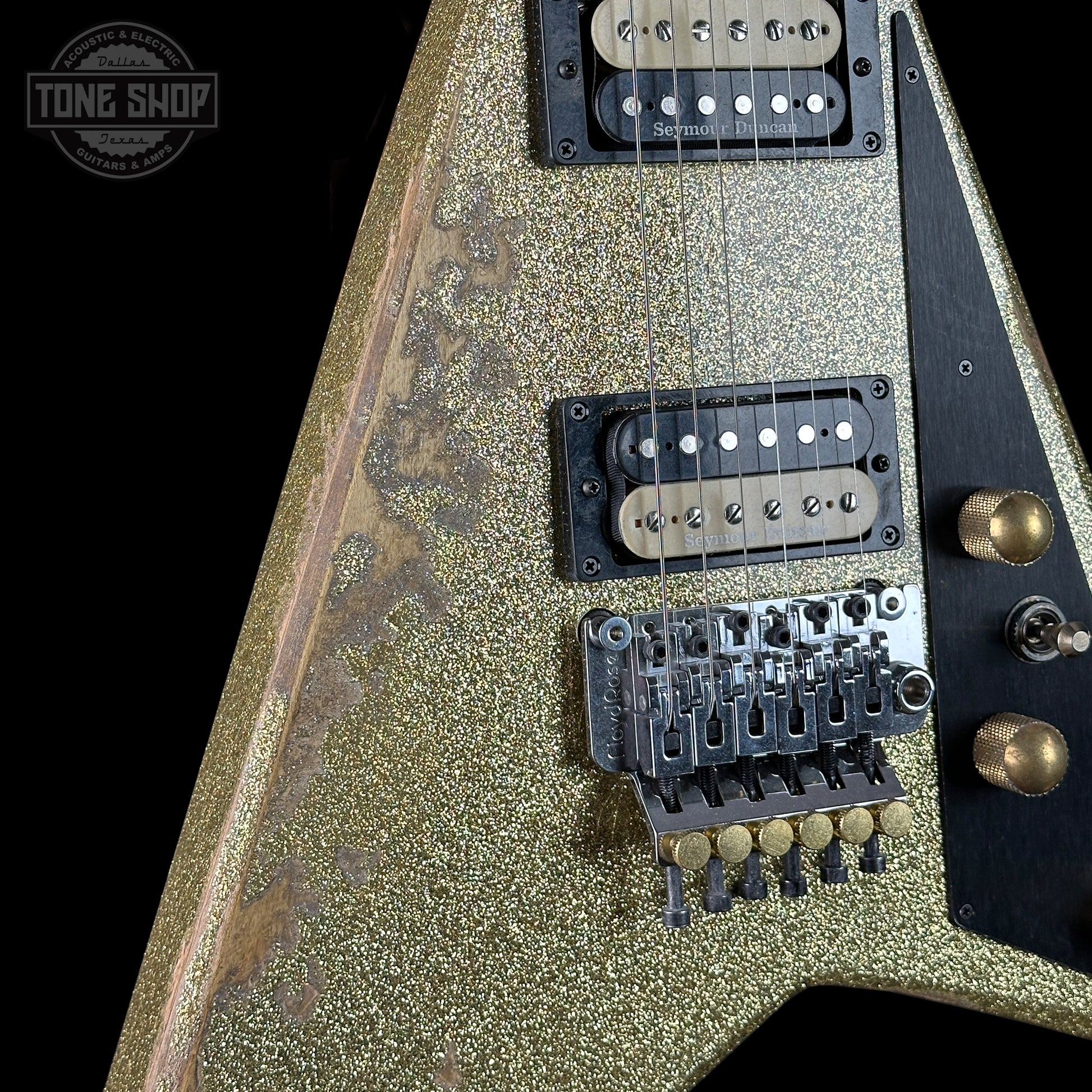 Close-up of a guitar with a glittery finish, pickups, and control knobs on a black background.