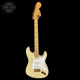 Beige electric guitar with a wooden neck on a black background, featuring 'Tone Shop' logo.