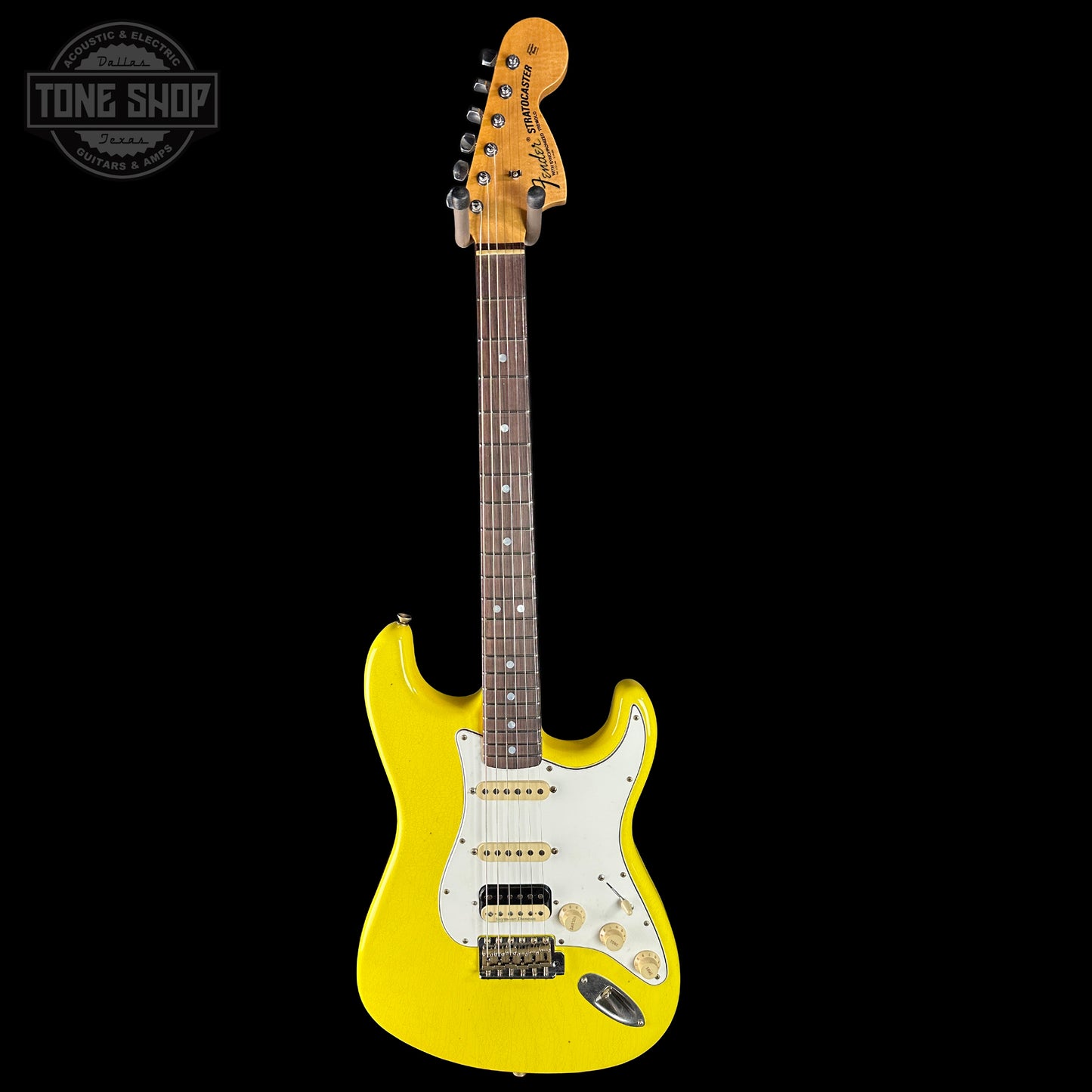 Yellow electric guitar with a white pickguard on a black background, featuring the Tone Shop logo.