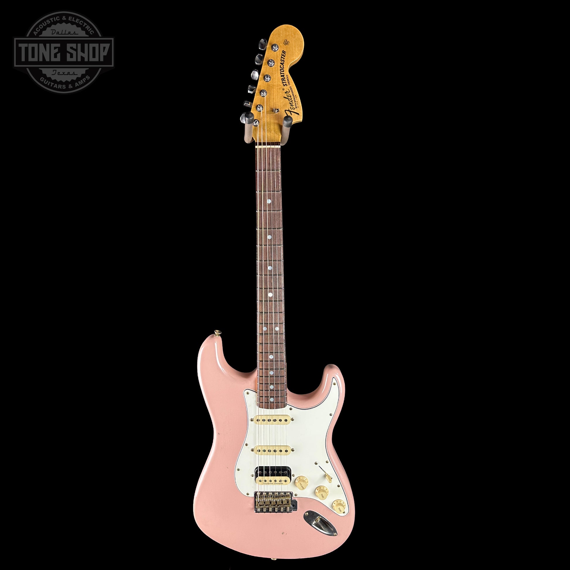 Pink electric guitar with a white pickguard on a black background, featuring the Tone Shop logo.