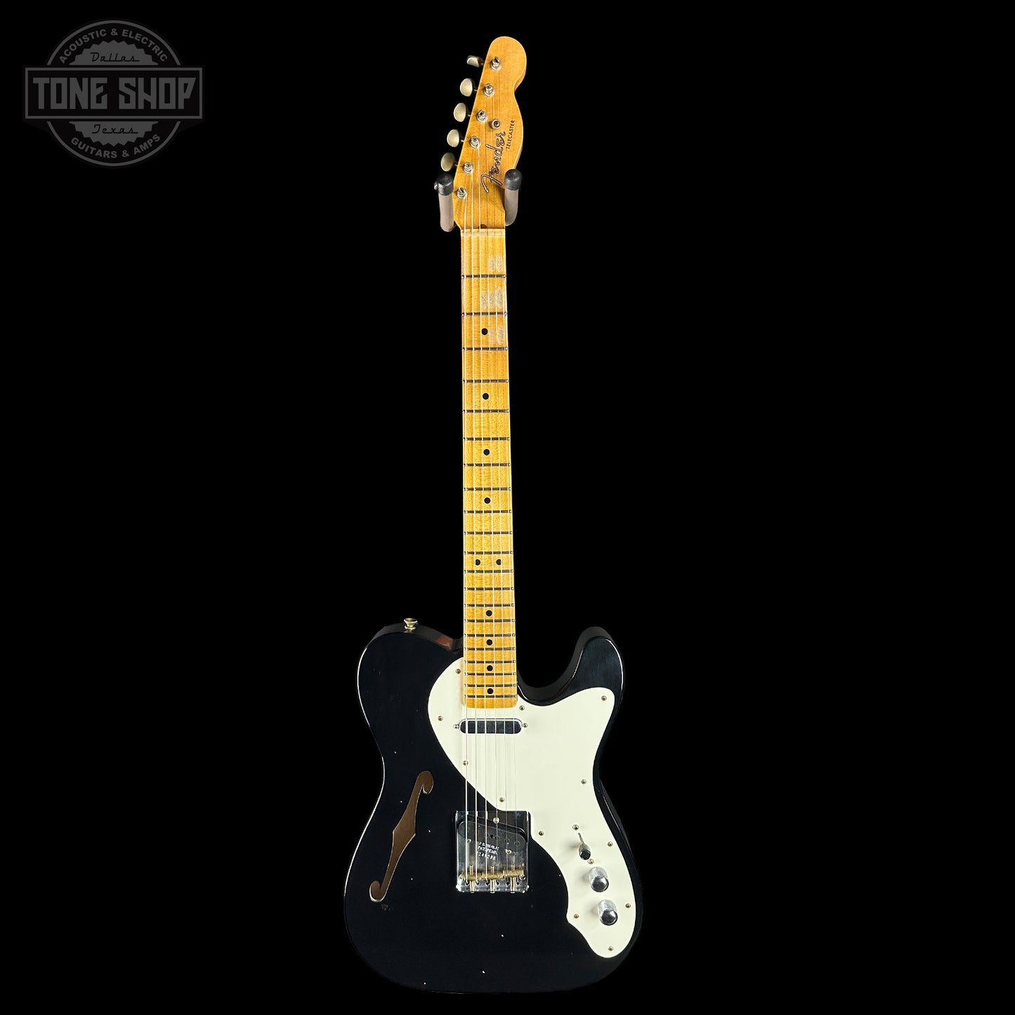 Electric guitar with a black body and white pickguard on a black background, featuring the Tone Shop logo.