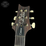 Guitar headstock with 'Custom' engraving on a black background, featuring the Tone Shop logo.