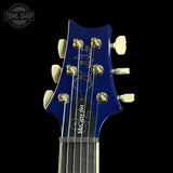 Close-up of a blue guitar headstock with 'Tone Shop' logo in the corner.