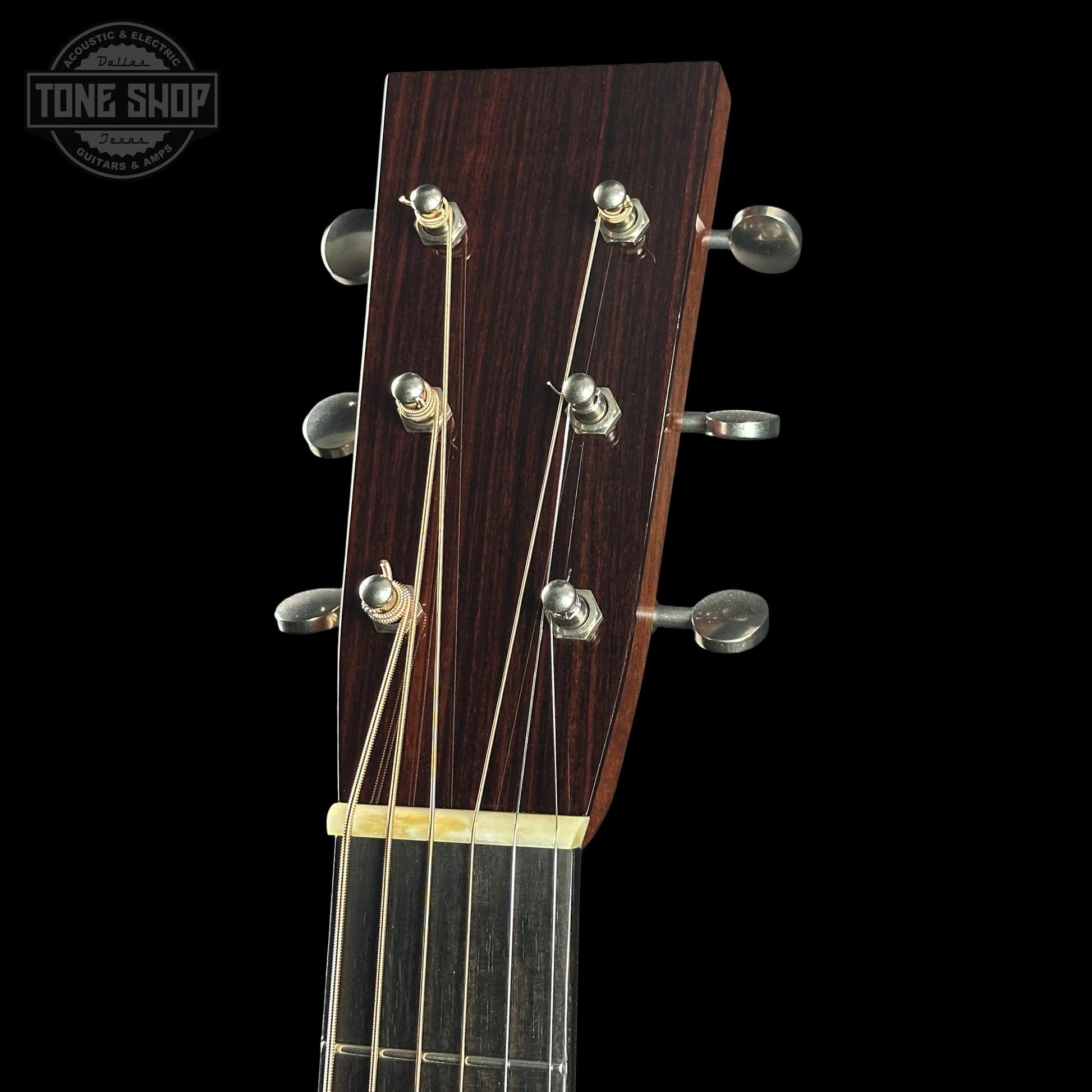 Close-up of a guitar headstock with tuning pegs on a black background, featuring the Tone Shop logo.