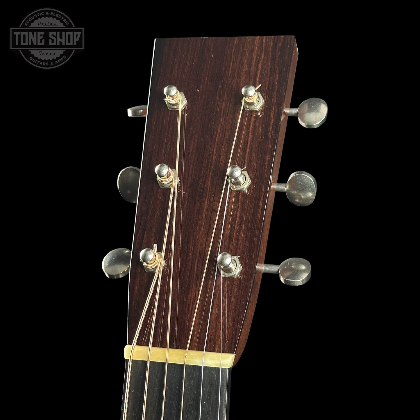 Close-up of a guitar headstock with tuning pegs on a black background, featuring the Tone Shop logo.