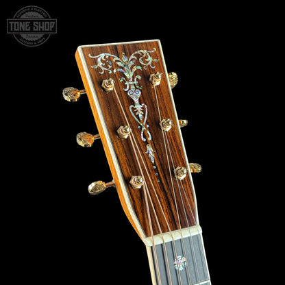 Close-up of a guitar headstock with intricate design on a black background, featuring the Tone Shop logo.