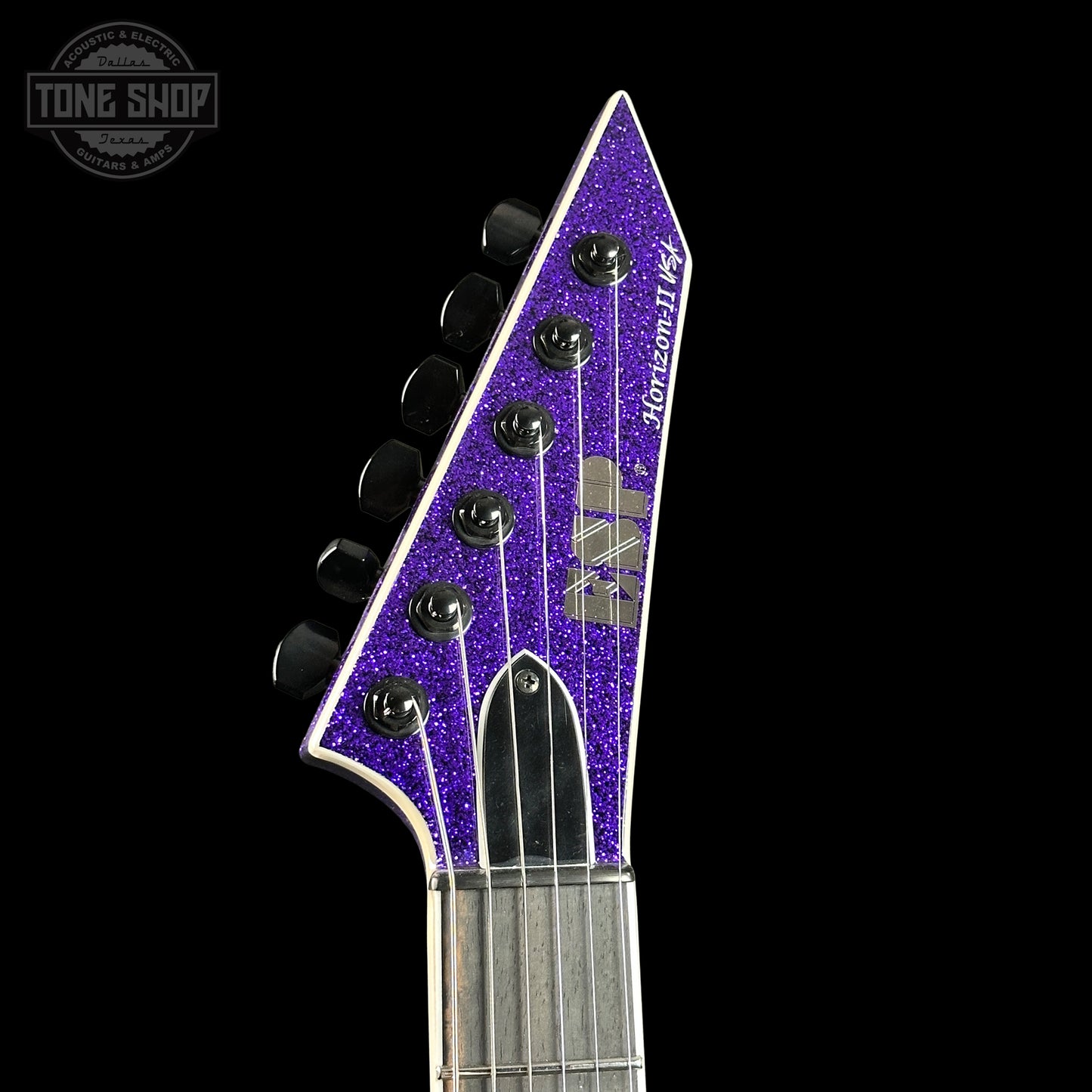 Close-up of a guitar headstock with purple glitter finish on a black background, featuring the 'Tone Shop' logo.