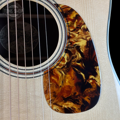 Close-up of a guitar's soundhole with a tortoiseshell pattern on a beige background.