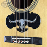 Close-up of an acoustic guitar with a longhorn skull design on the pickguard.