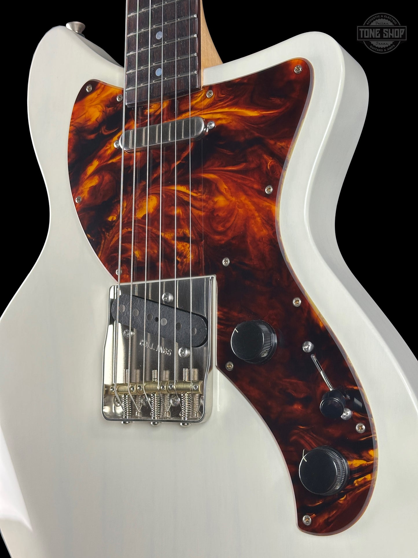 White electric guitar with a tortoiseshell pickguard on a black background