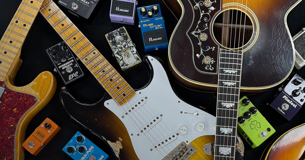 A group of guitars and pedals on a black background.